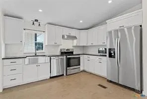 Modern kitchen featuring white cabinetry, dark countertops, a stainless steel farmhouse sink, and stainless steel appliances