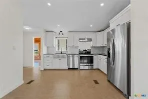 Kitchen featuring white cabinetry, dark countertops, stainless steel appliances, and wood-finish flooring