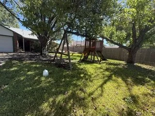Expansive grassy area with mature trees, a wooden fence, and a partial view of the property's exterior with a garage
