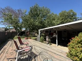 Expansive wood-finish deck with a covered patio structure, mature trees, and privacy fencing