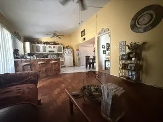 Open-concept living area with wood-finish flooring, a kitchen island with seating, white cabinetry, and a ceiling fan