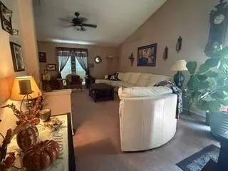 Vaulted ceiling in a spacious living area featuring carpet flooring, ceiling fan, and window with dark drapes