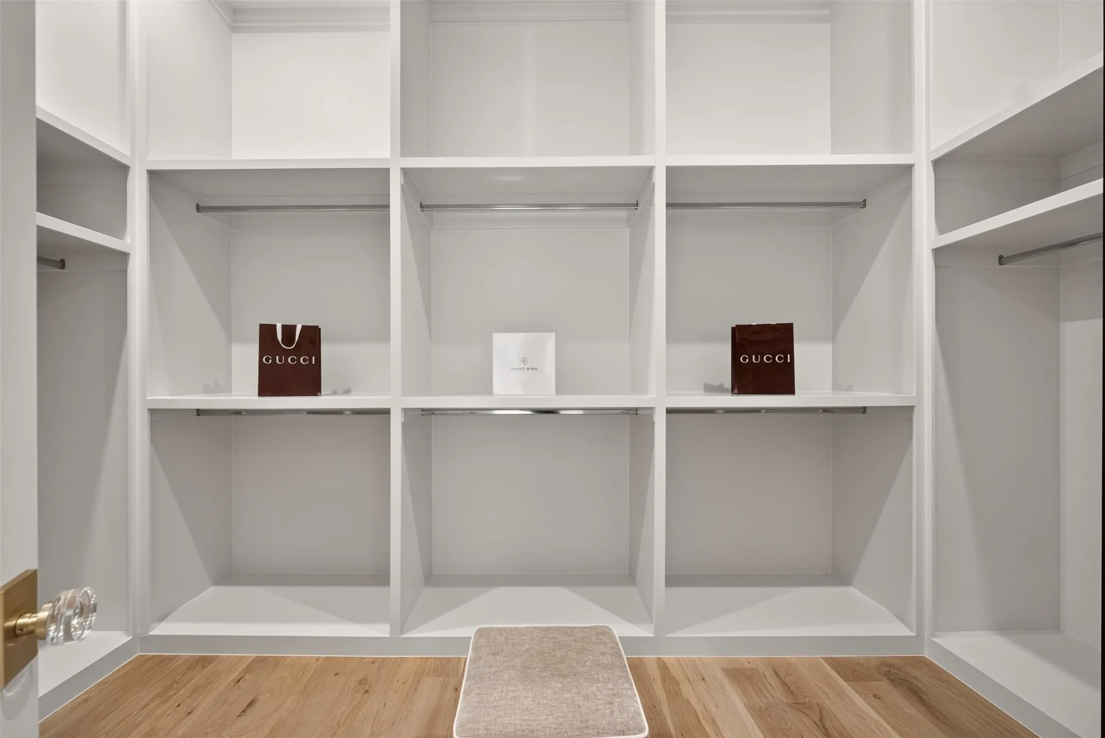 Built-in white shelving, integrated hanging rods, wood-finish flooring, and a crystal-knob door handle