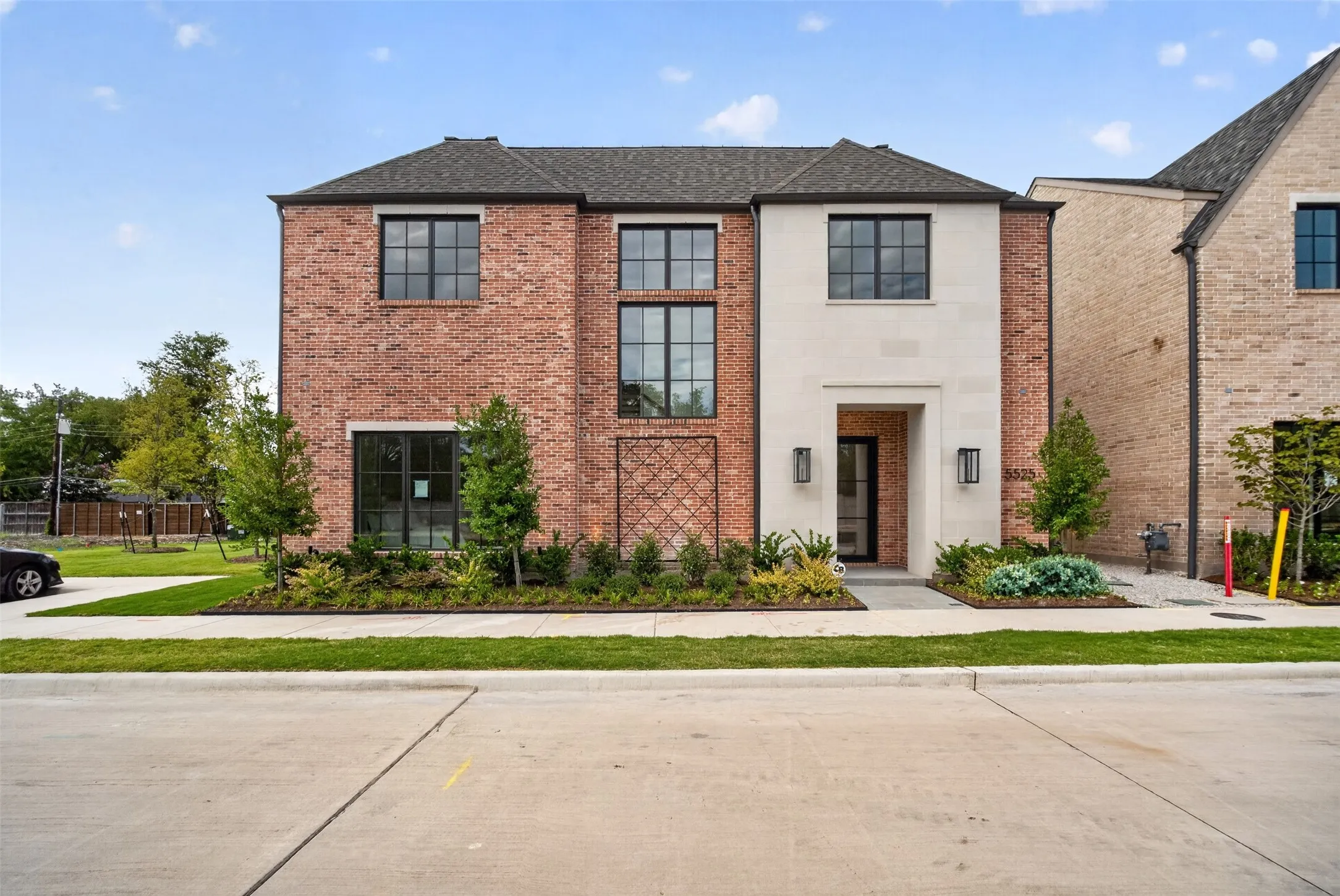 Brick and stone facade with dark-framed windows, a prominent entryway, a landscaped front yard, and a concrete walkway