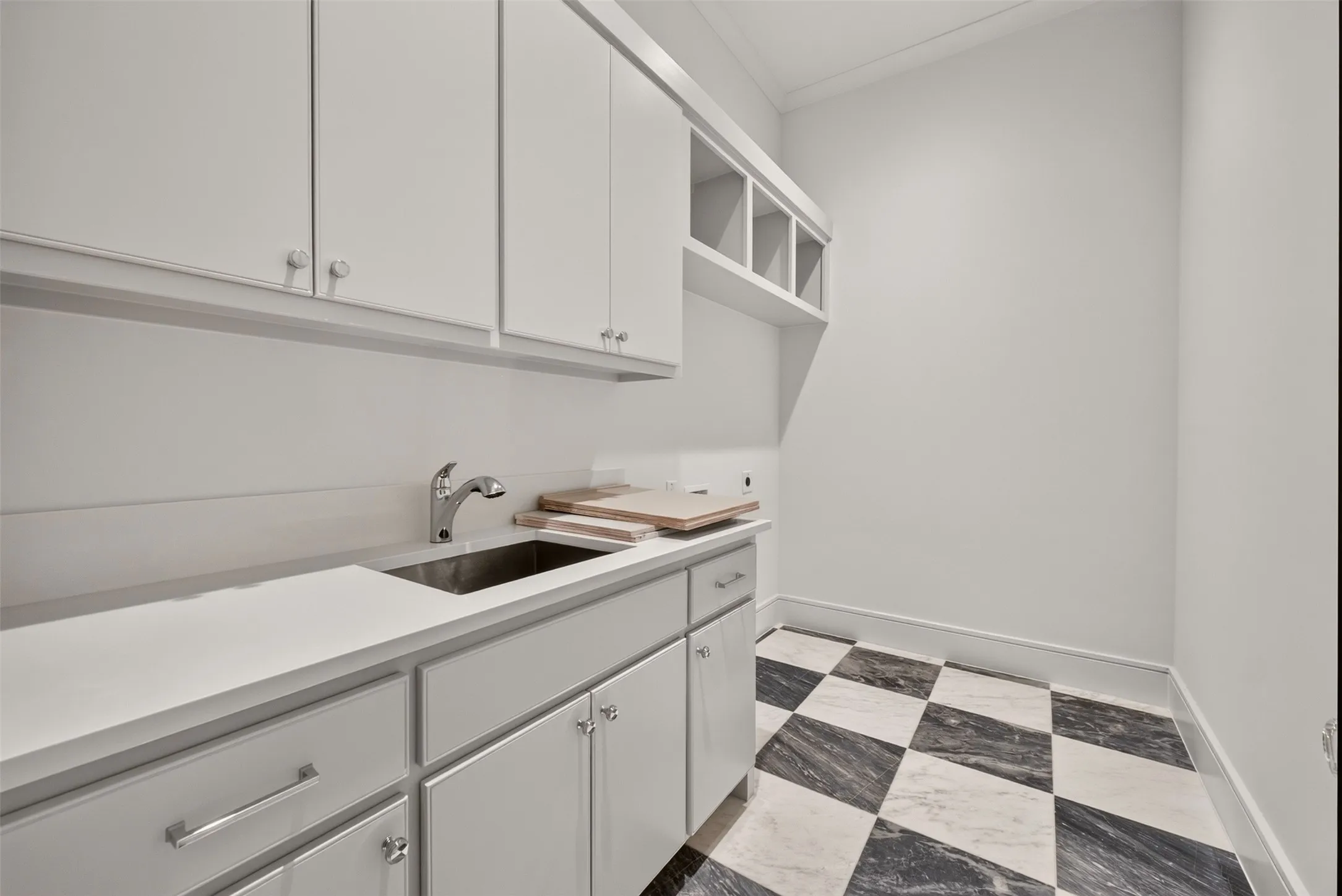 White cabinetry, a stainless steel sink, a chrome faucet, and a black and white checkerboard floor