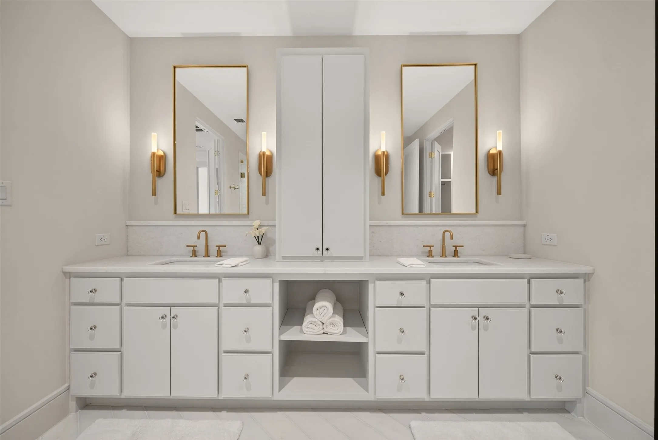 Dual vanity with white cabinetry, gold-finish hardware, rectangular undermount sinks, and wall-mounted sconces