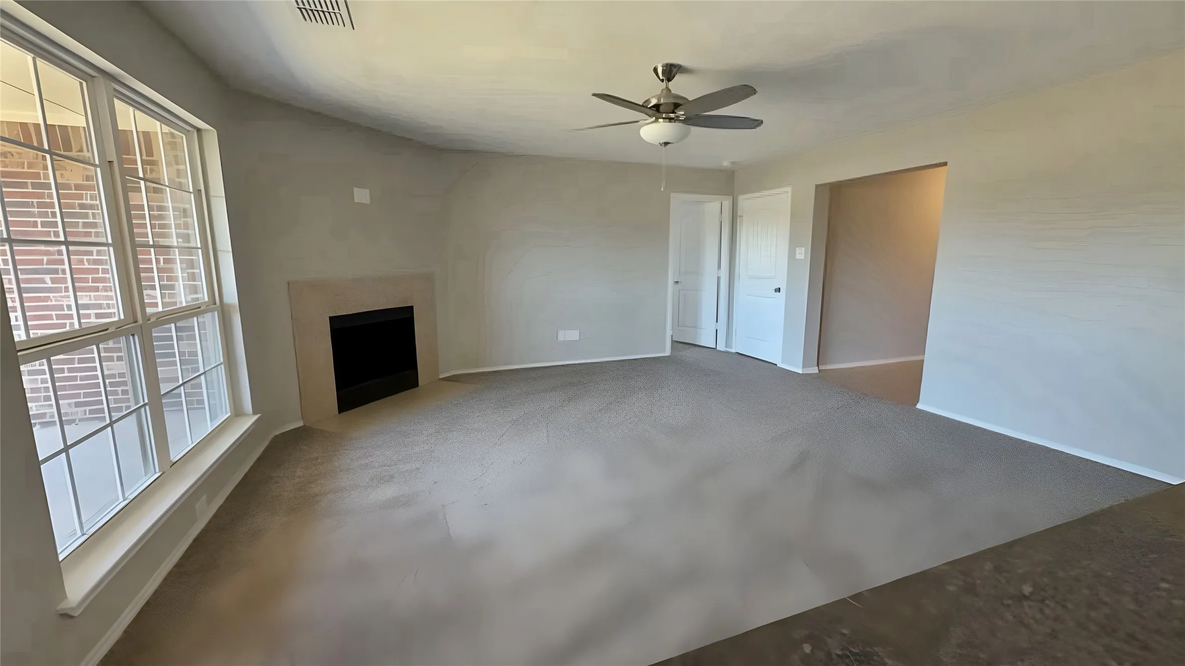 Spacious room with carpeted flooring, a corner fireplace with a light-toned surround, an overhead ceiling fan, and large multi-pane windows