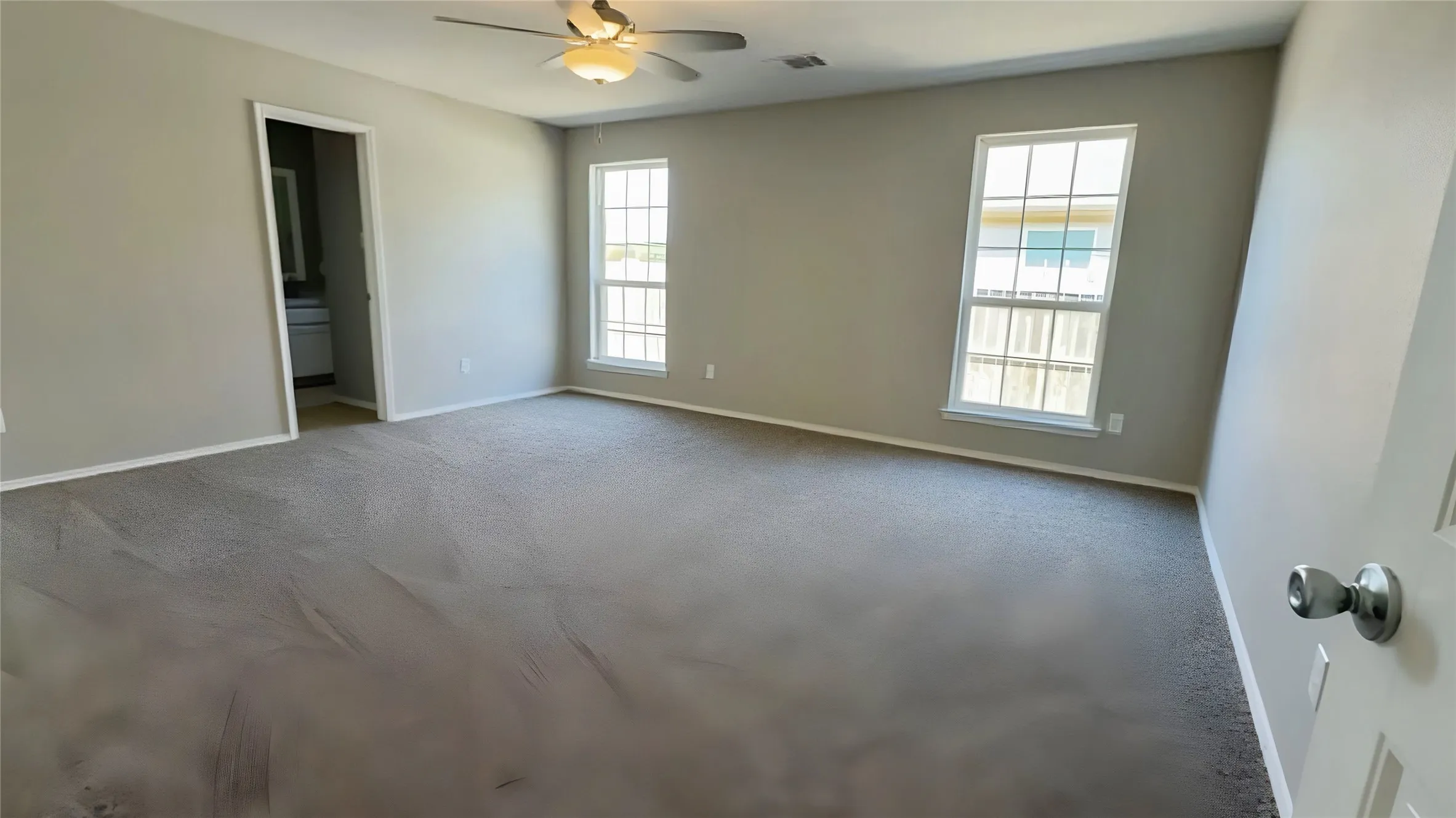 Spacious room featuring neutral carpeting, light gray wall paint, and a ceiling fan with integrated lighting