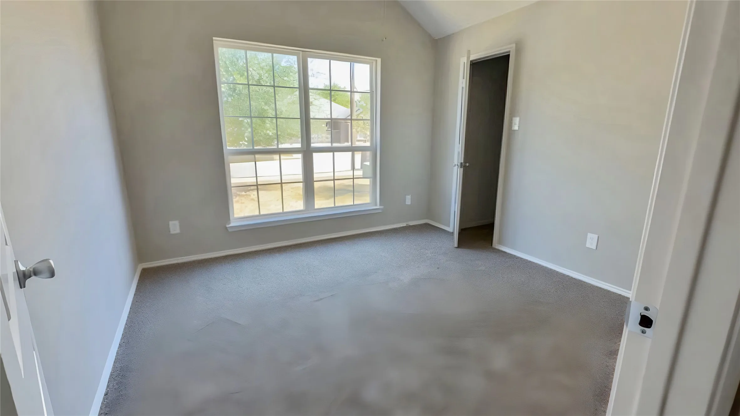 Vaulted ceiling, light neutral wall color, window with grid pattern, neutral carpeting, white trim