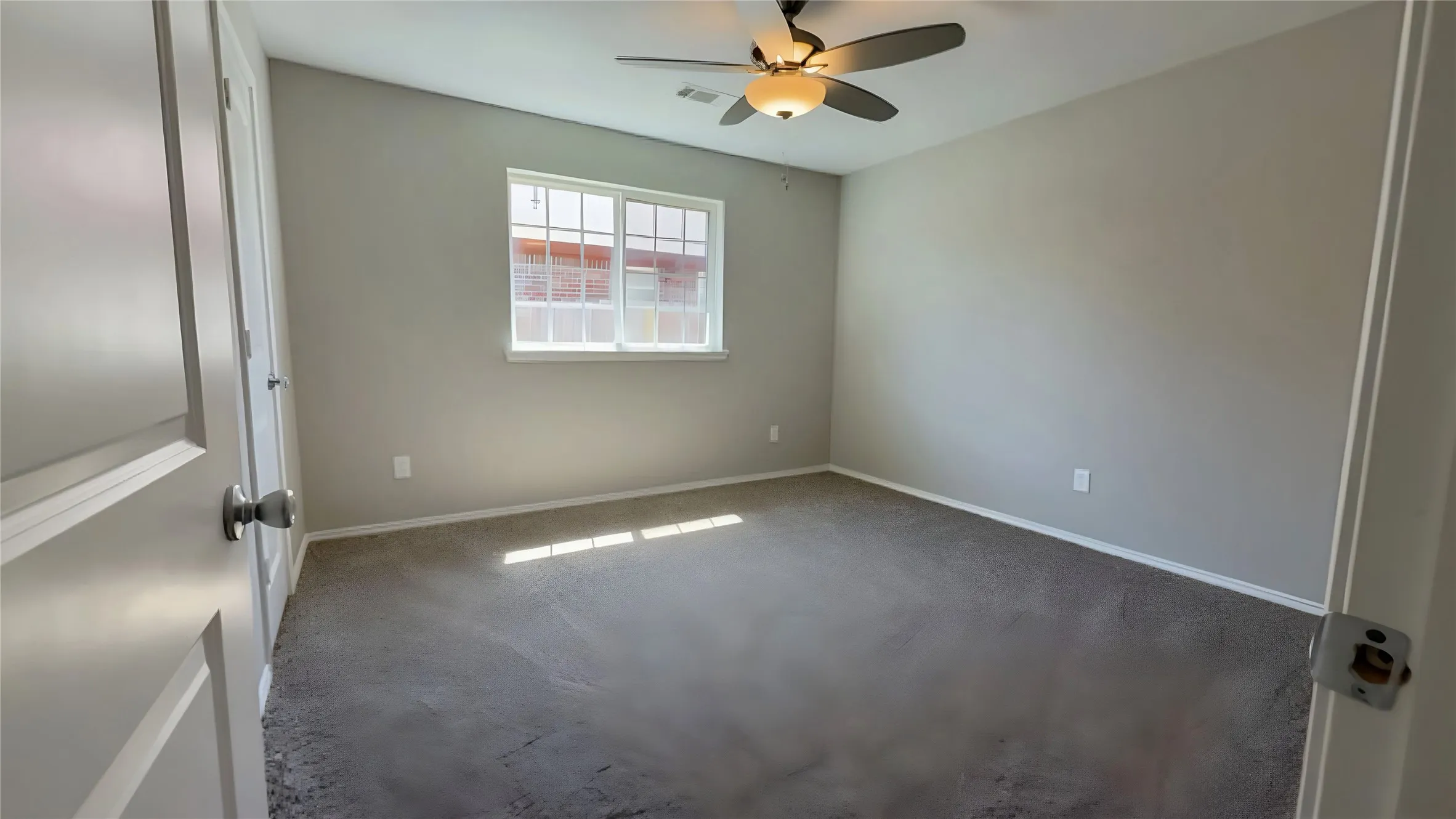 Neutral-toned walls, gray carpeting, a multi-pane window, and a ceiling fan with integrated lighting