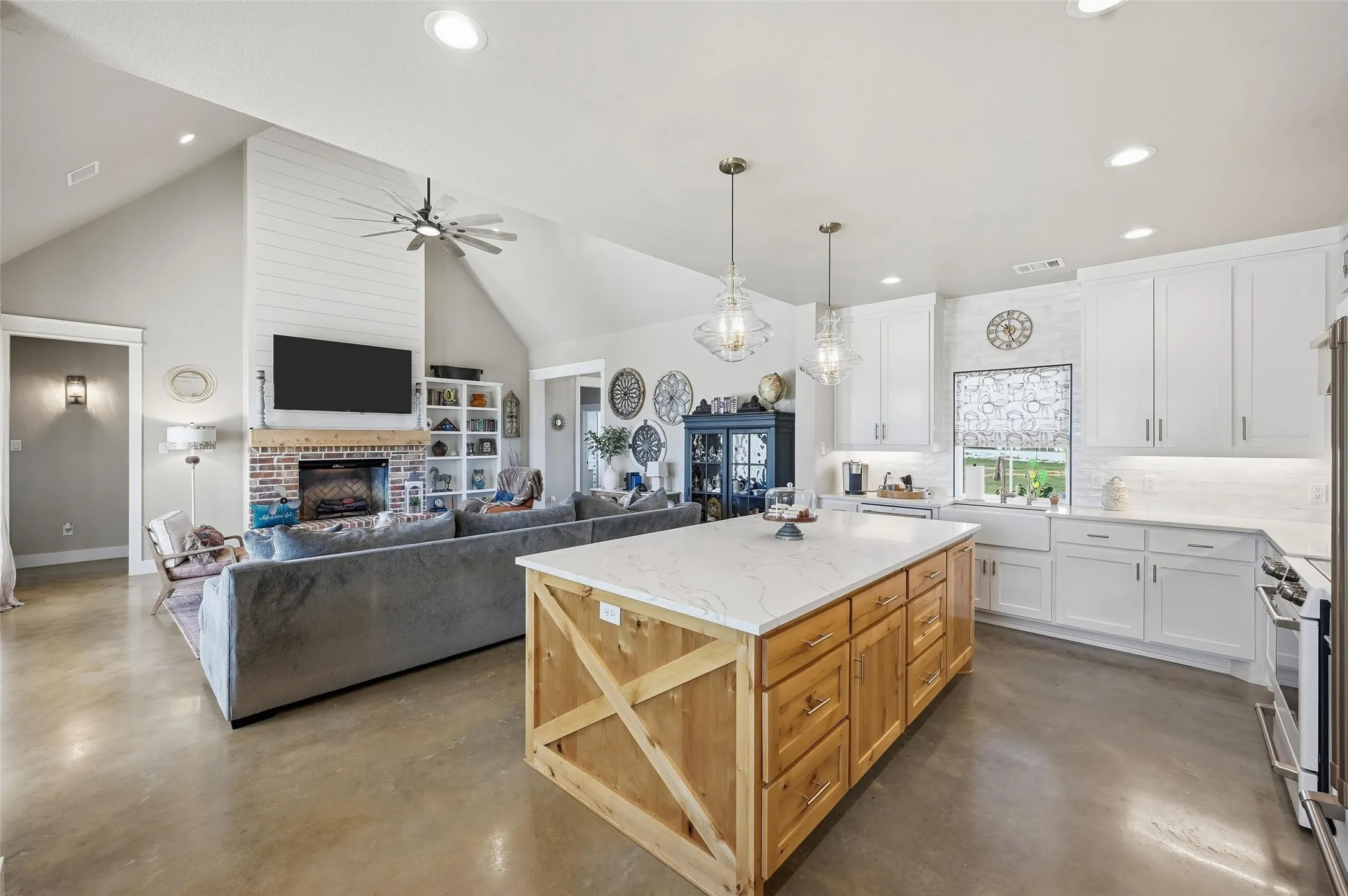Kitchen featuring white cabinetry, a brick fireplace, concrete floors, decorative backsplash, and high vaulted ceiling