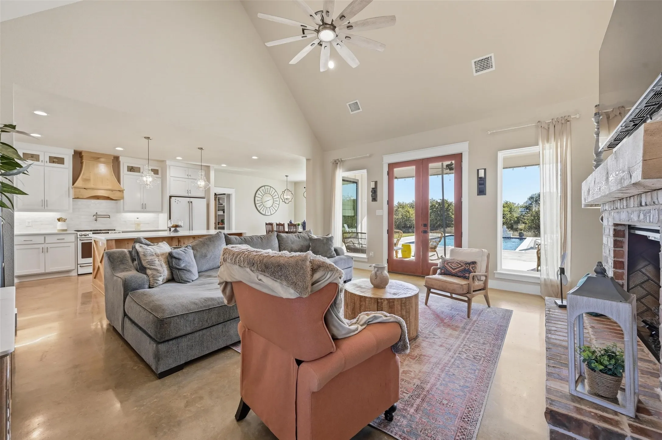 Living room with high vaulted ceiling, ceiling fan, french doors, finished concrete flooring, and a fireplace