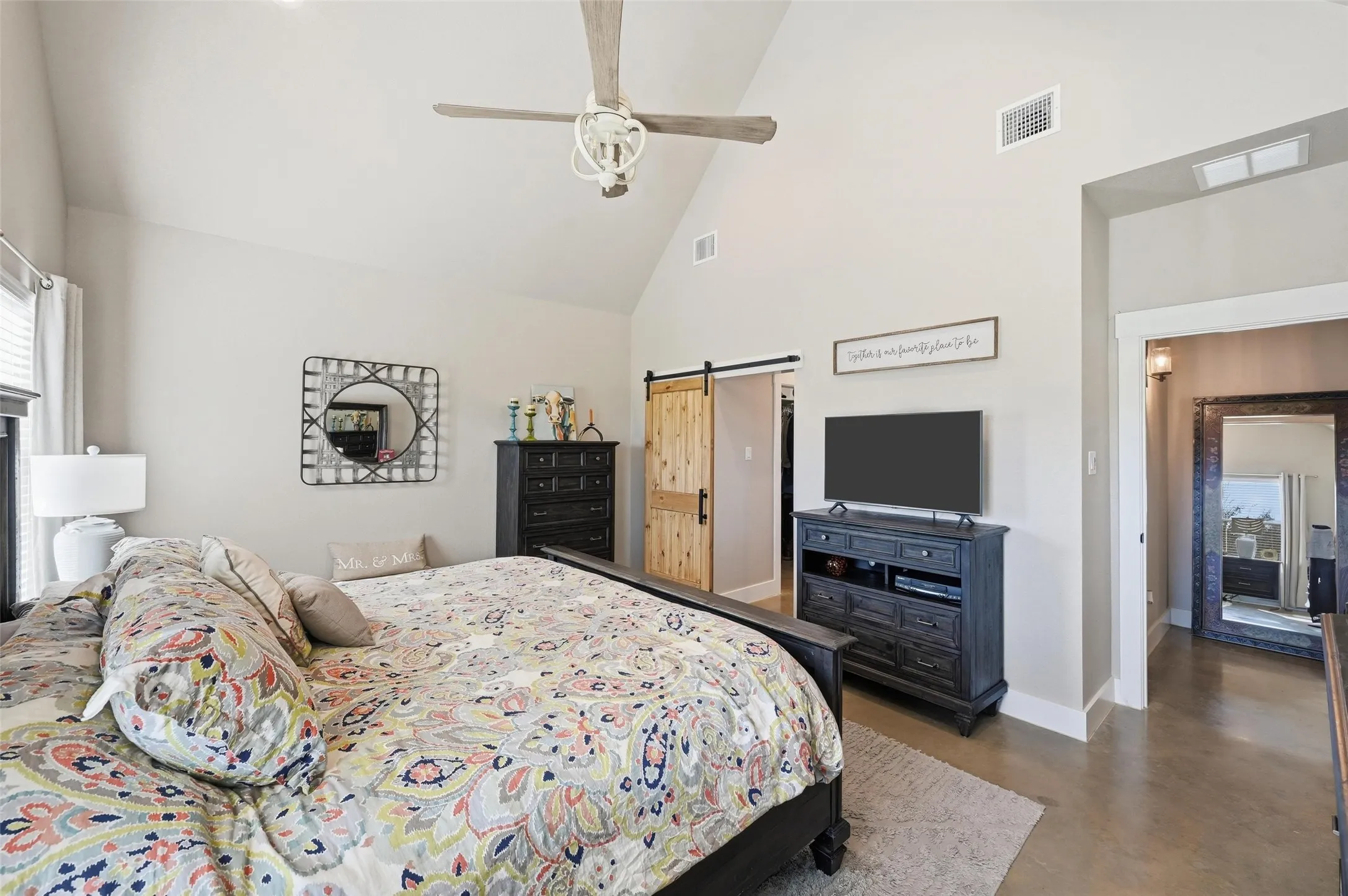 Bedroom featuring a barn door, high vaulted ceiling, finished concrete flooring, and ceiling fan