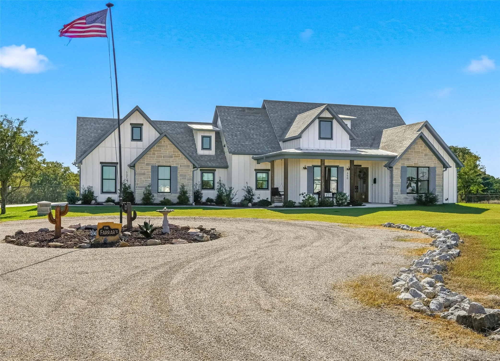 Modern inspired farmhouse with board and batten siding, stone siding, covered porch, roof with shingles, and circular driveway