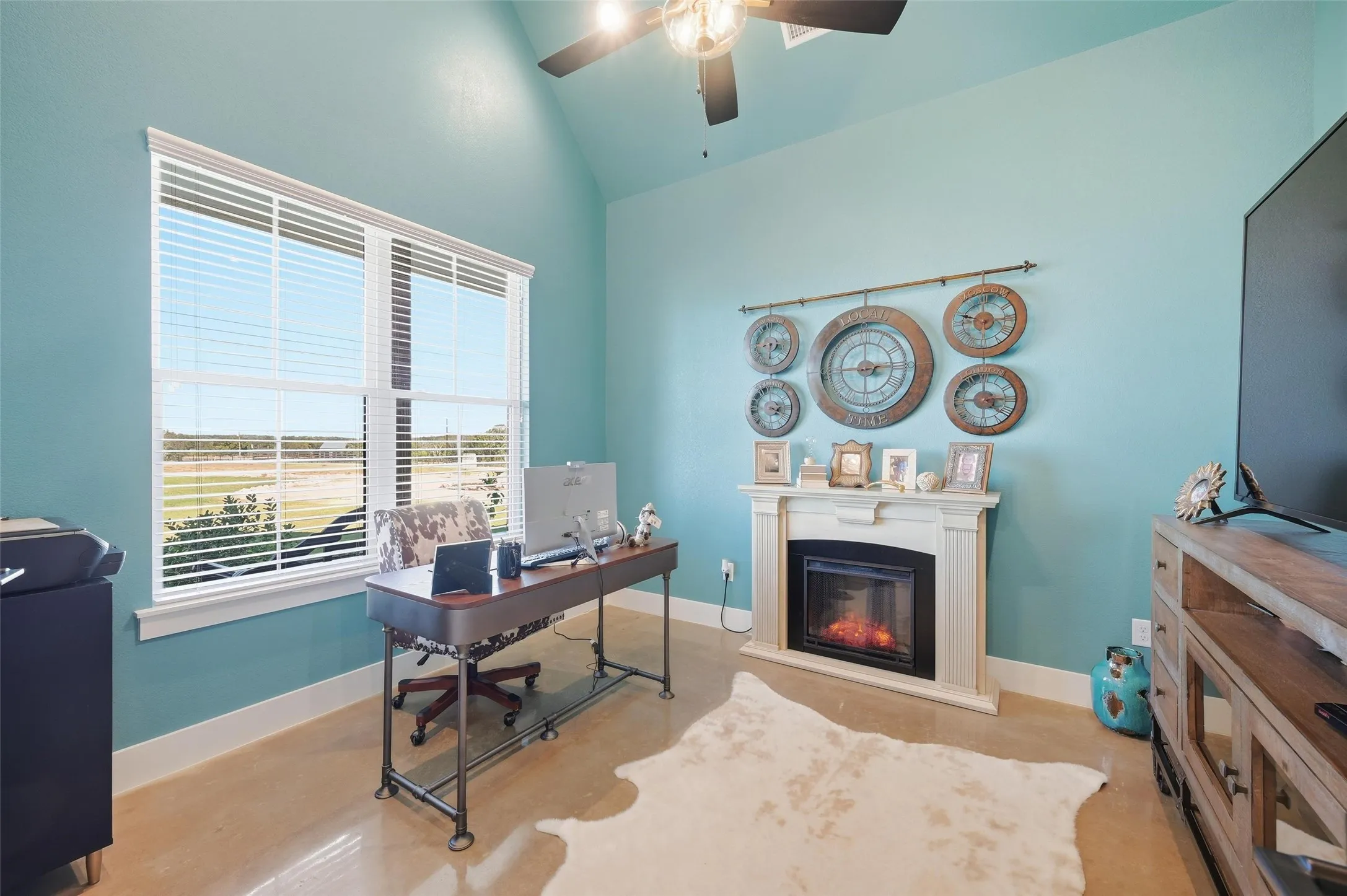 Home office featuring vaulted ceiling, a glass covered fireplace, and ceiling fan