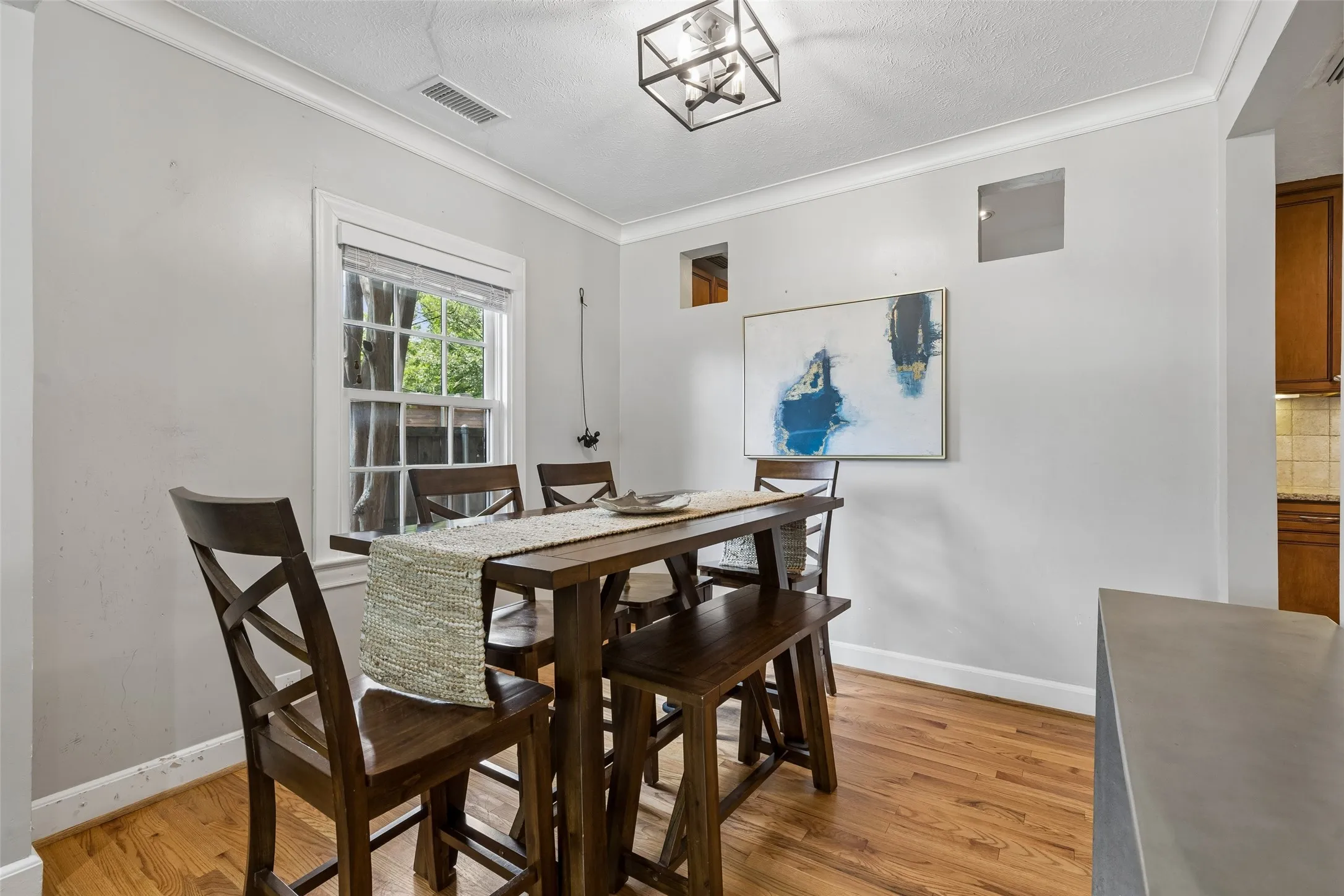 Hardwood flooring with white crown molding, a large double-hung window, and an attached ceiling fixture