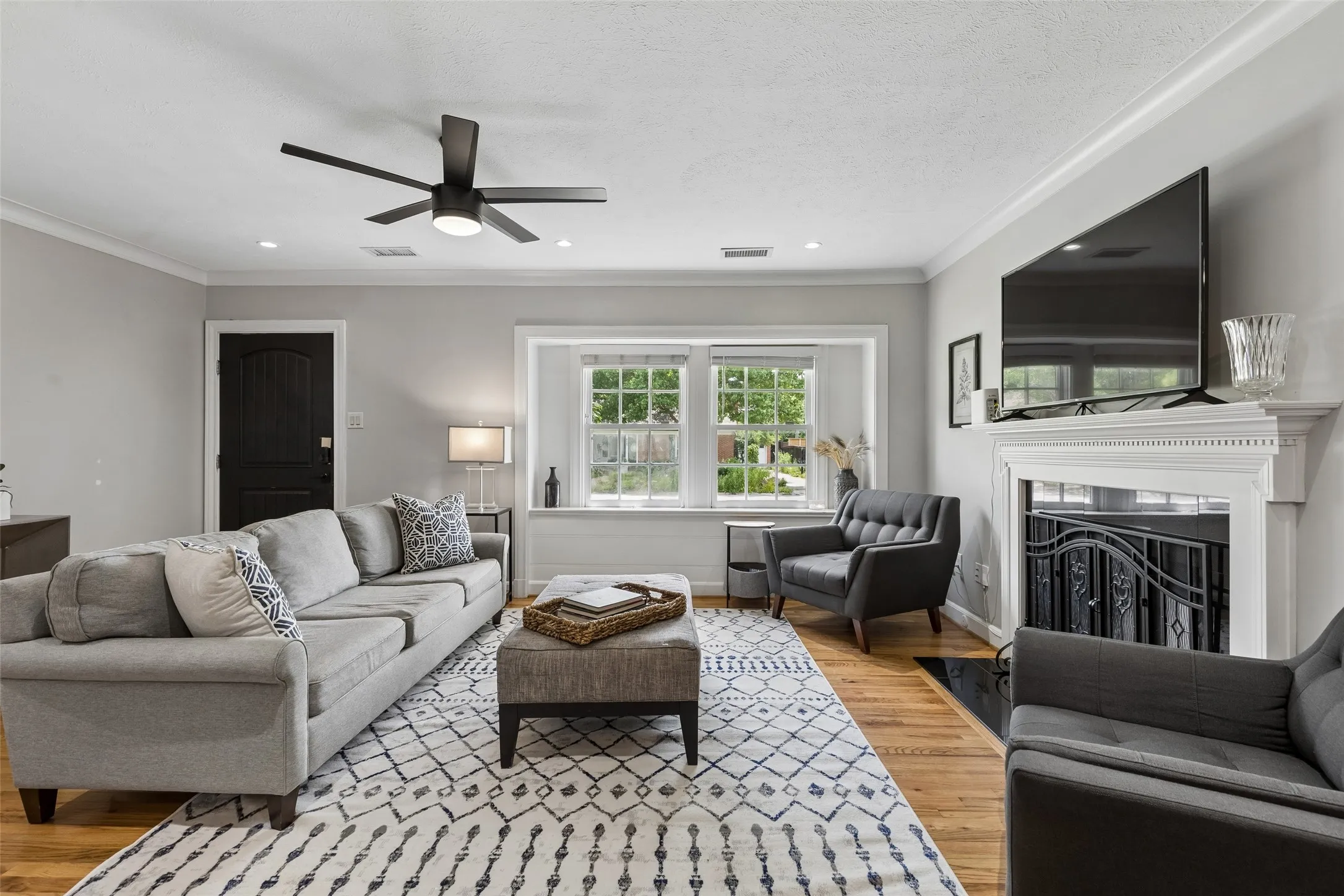 Hardwood flooring extending throughout, a decorative fireplace with an ornate screen, a bay window with a window seat, recessed lighting, and a ceiling fan with integrated illumination