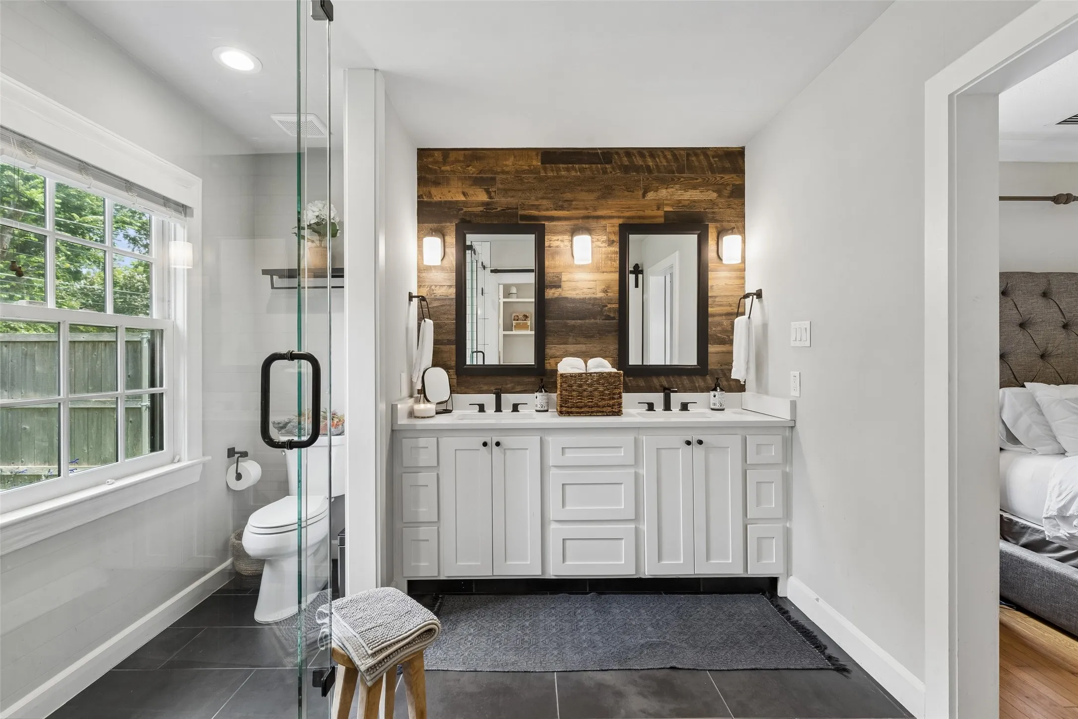 Dual vanity with white shaker-style cabinetry, wood-finish accent wall, and glass-enclosed shower