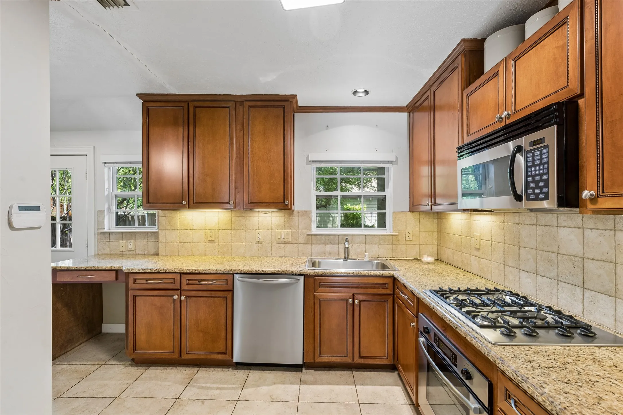 Kitchen featuring wood cabinetry, light-colored countertops, stainless steel appliances, tile flooring, and a tile backsplash