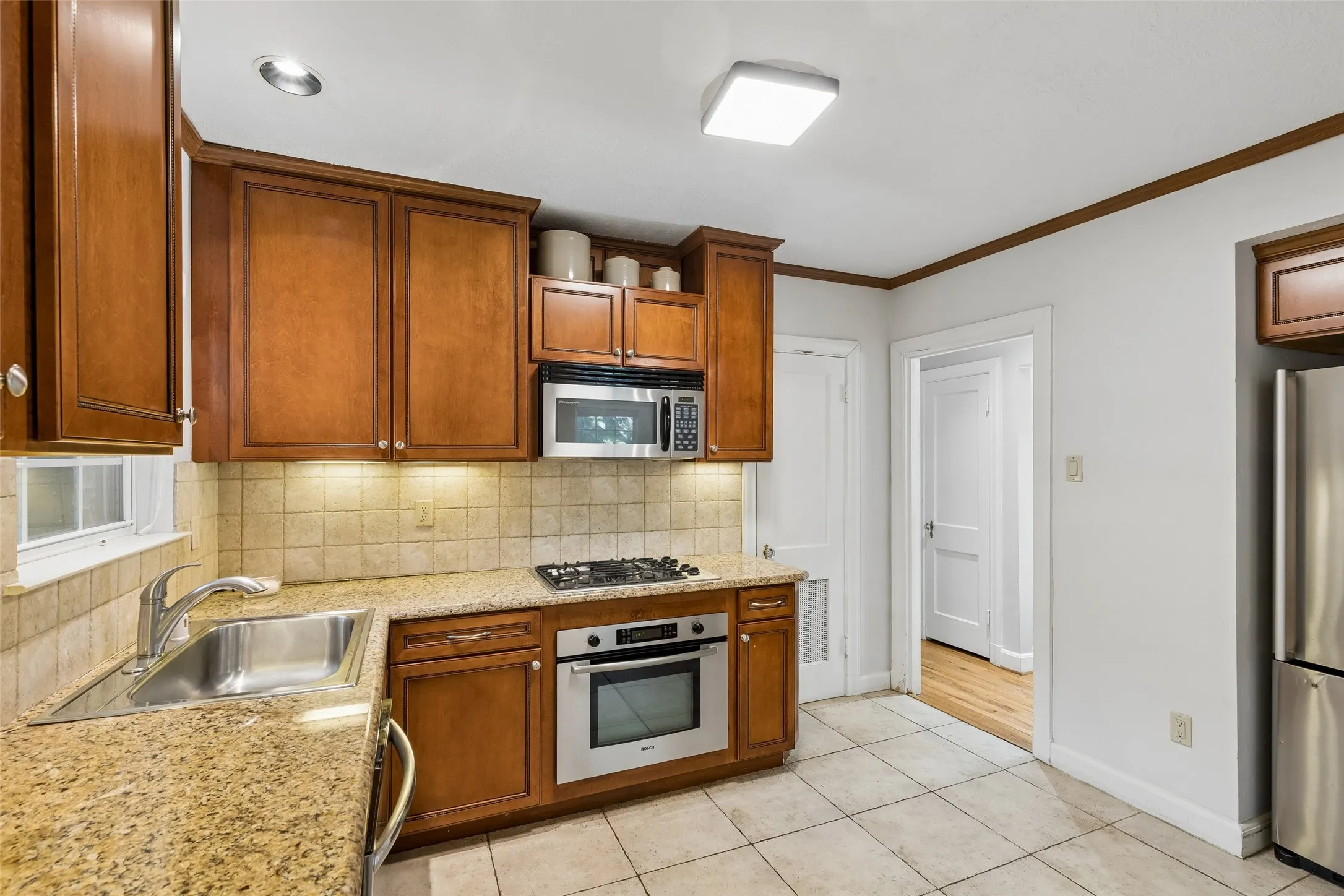 Kitchen featuring wood cabinetry, stainless steel appliances, speckled stone countertops, tile flooring, and a tile backsplash