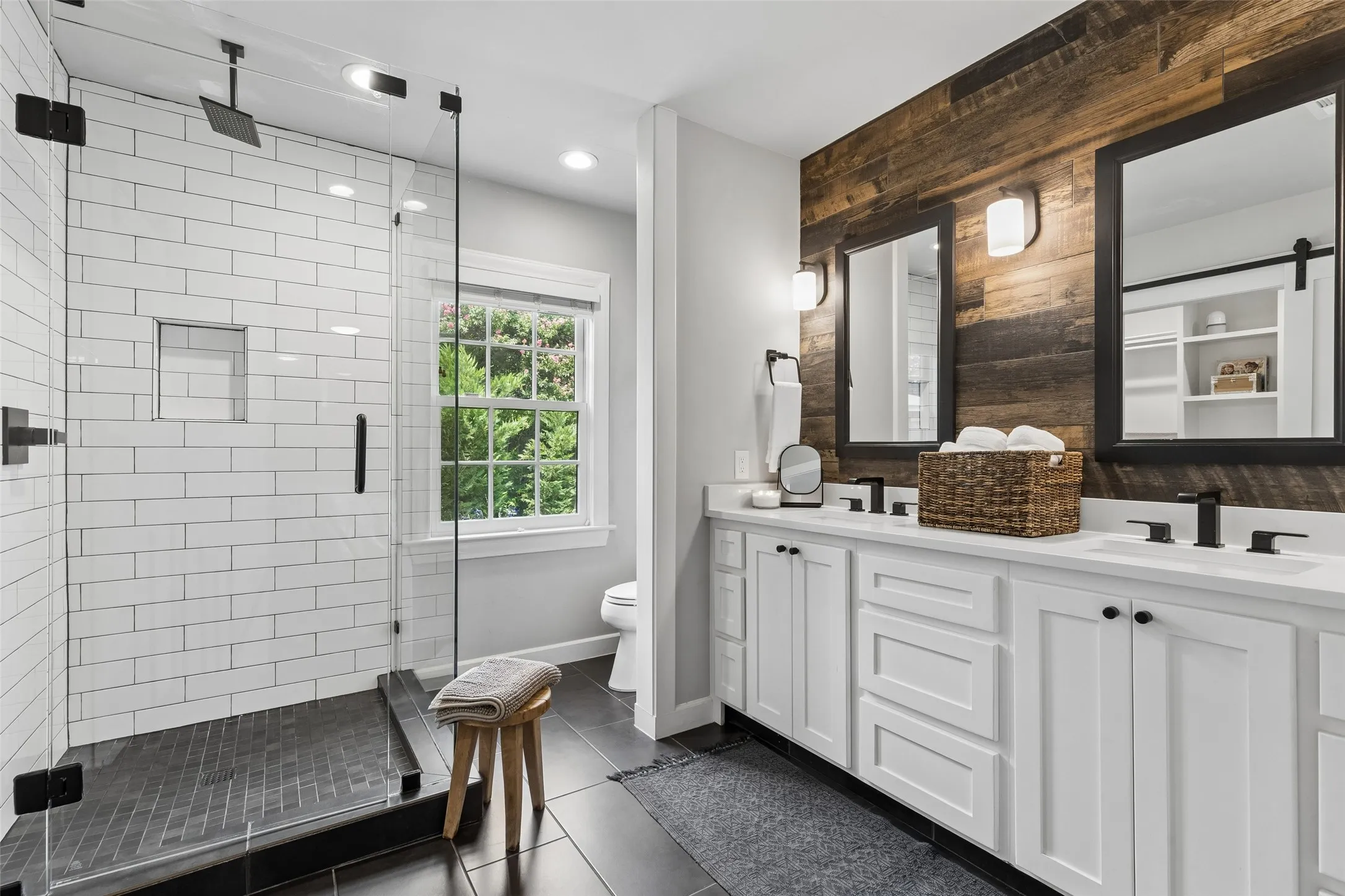 Dual vanity with white cabinetry and integrated sinks, wood-finish accent wall, and matte black fixtures