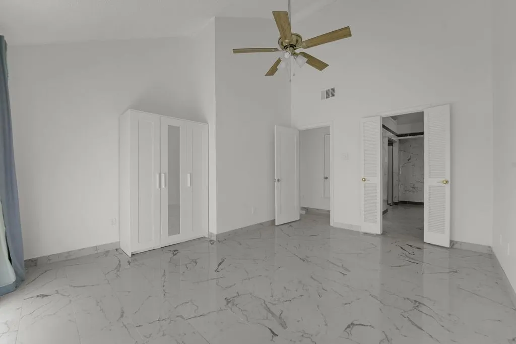 Vaulted ceiling with ceiling fan, white paneled doors, and polished tile flooring