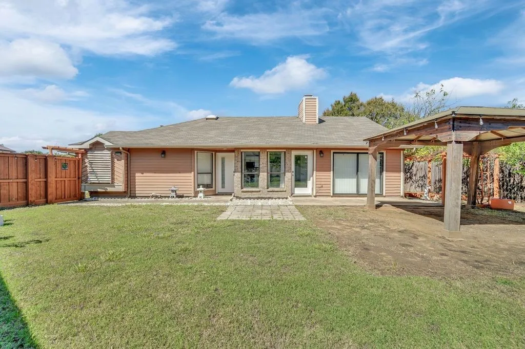 Rear exterior featuring peach-toned siding, a multi-panel sliding glass door, a wood-finish pergola, and a privacy fence