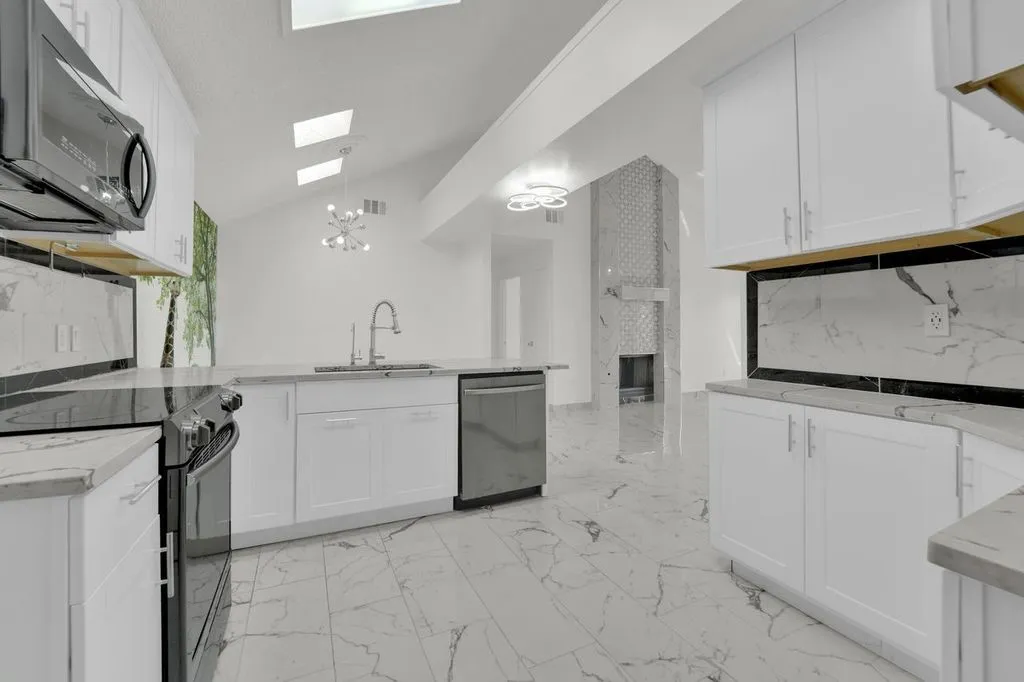 Vaulted ceiling with skylights, white cabinetry, integrated stainless steel appliances, light-toned flooring, and a decorative fireplace