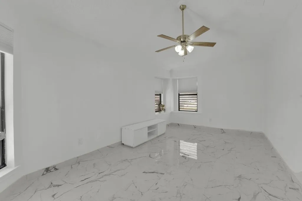 Recessed window with horizontal blinds, polished tile flooring with natural stone-look veining, and a ceiling fan with light fixture