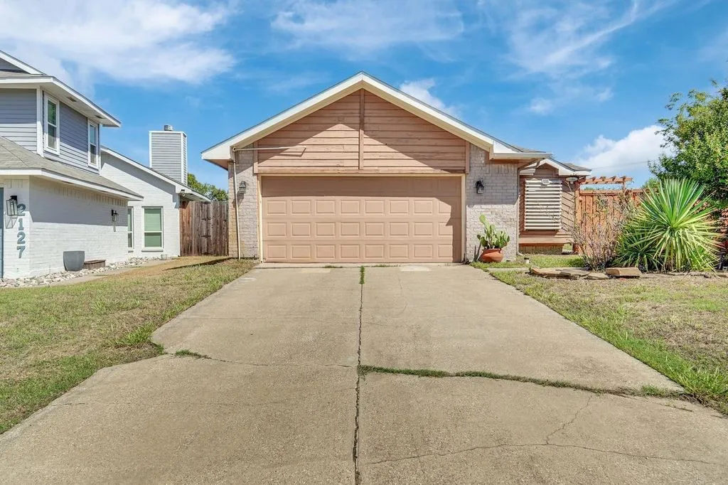 Attached garage with a neutral-toned door, brick facade, and wood-finish siding details
