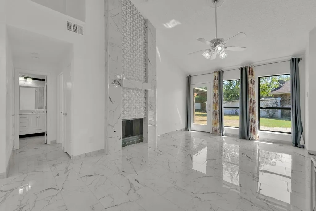 Vaulted ceiling with a ceiling fan, fireplace with a decorative surround, large windows, and reflective tile flooring