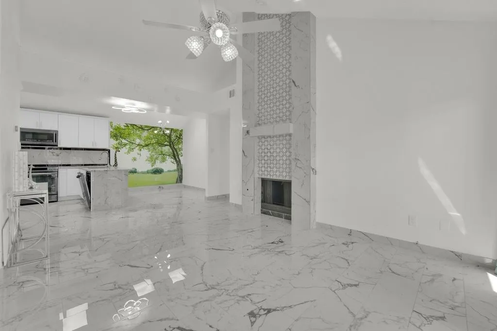 Vaulted ceiling with an attached ceiling fan, floor-to-ceiling fireplace with decorative tile accents, large format tile flooring, white cabinetry, and a kitchen island with a built-in dishwasher