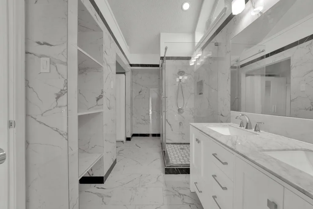 Dual vanity with integrated sinks, full-width mirror, glass-enclosed shower, and built-in shelving
