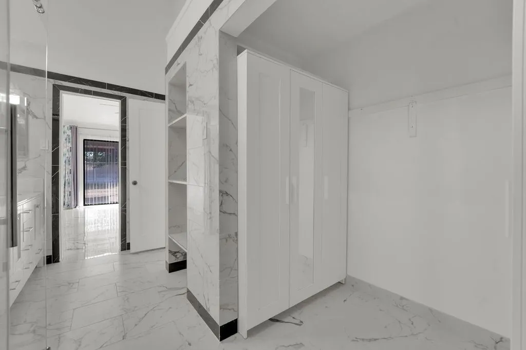 White marble-look floor tiles, built-in shelving, white door, and white painted walls