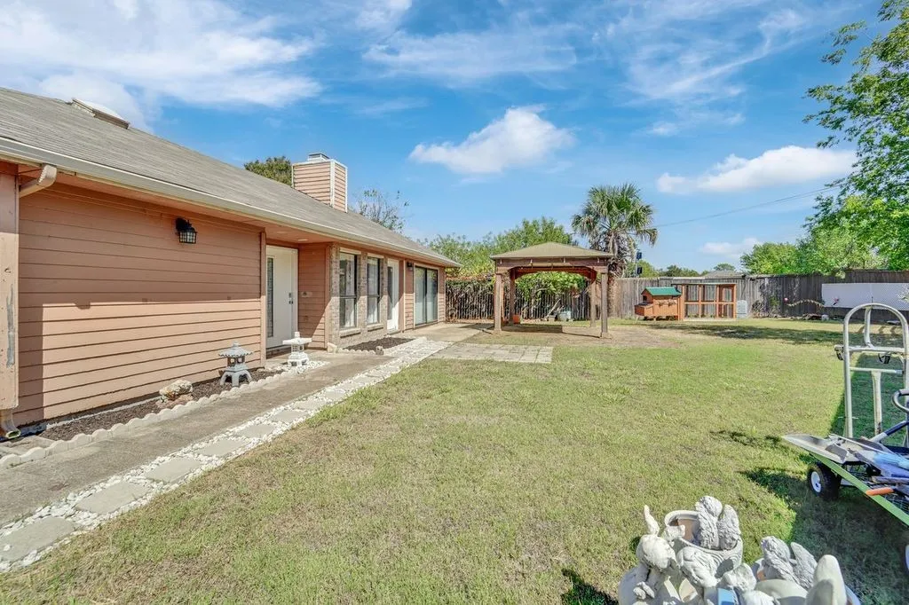 Expansive backyard featuring a gazebo with a stone paver base, a single-story residence with horizontal siding, and a stone pathway