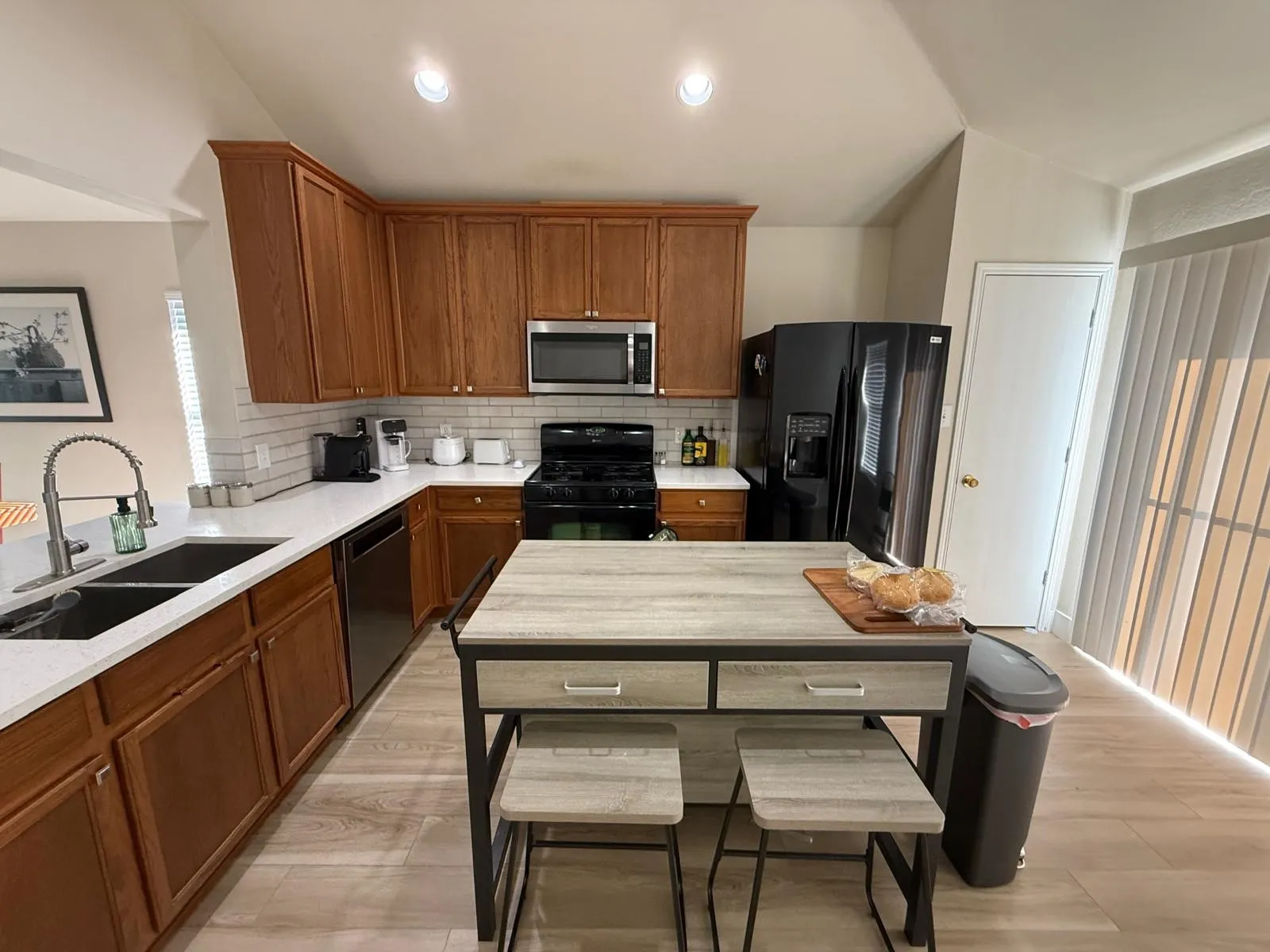 Kitchen featuring wood-finish cabinetry, stainless steel appliances, a white subway tile backsplash, and light-toned wood-finish flooring
