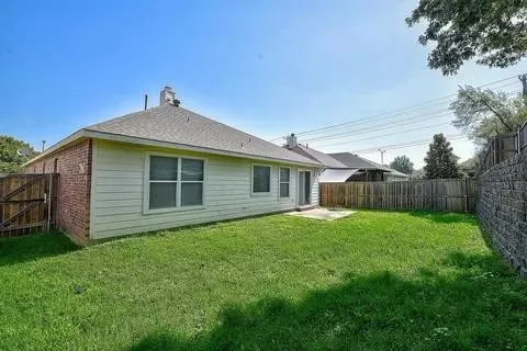 Spacious single-story brick and siding residence with expansive manicured lawn, mature landscaping, and wooden privacy fencing