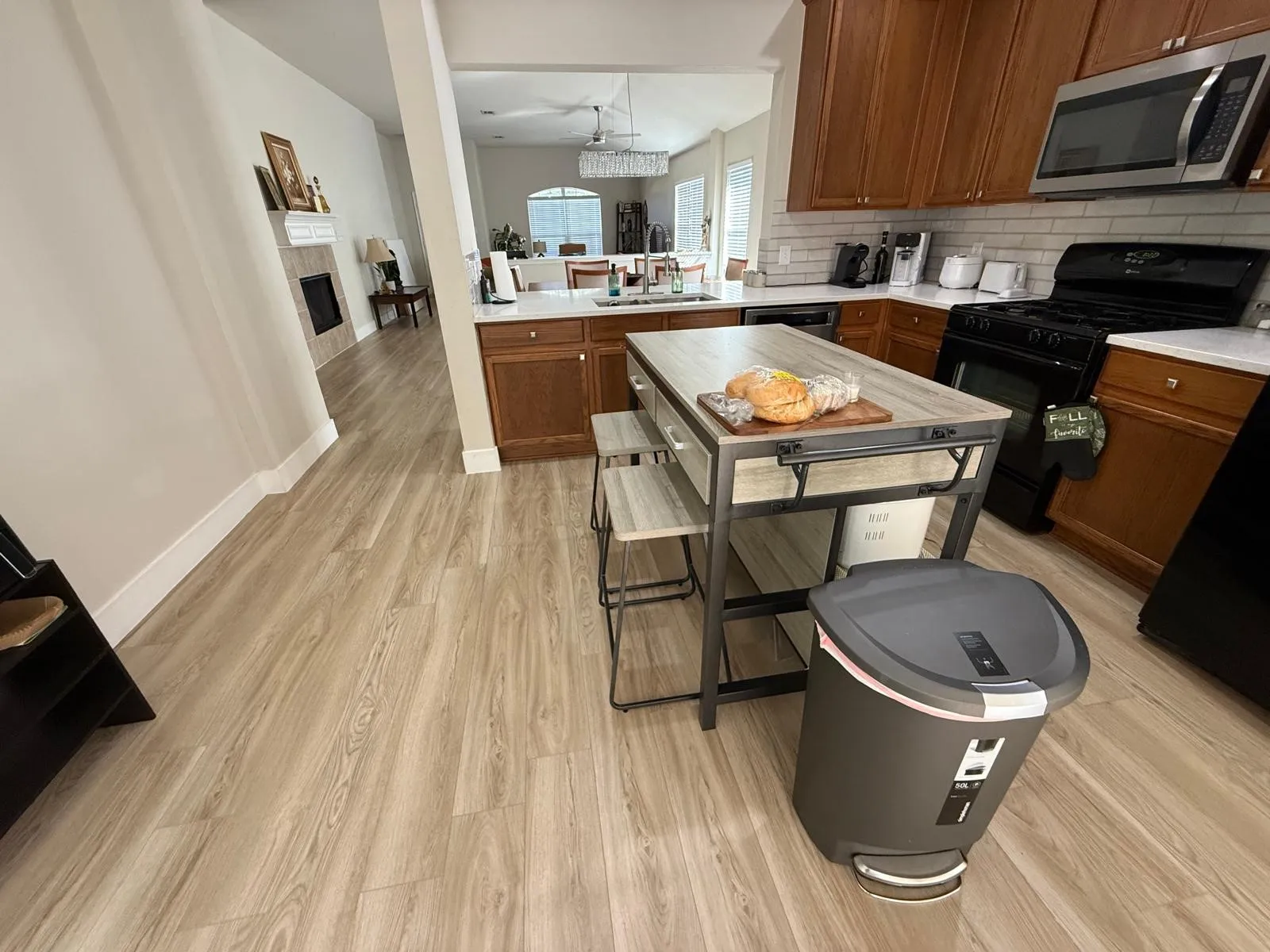 Wood-finish flooring throughout, kitchen featuring wood cabinetry, white countertops, tile backsplash, and stainless steel appliances