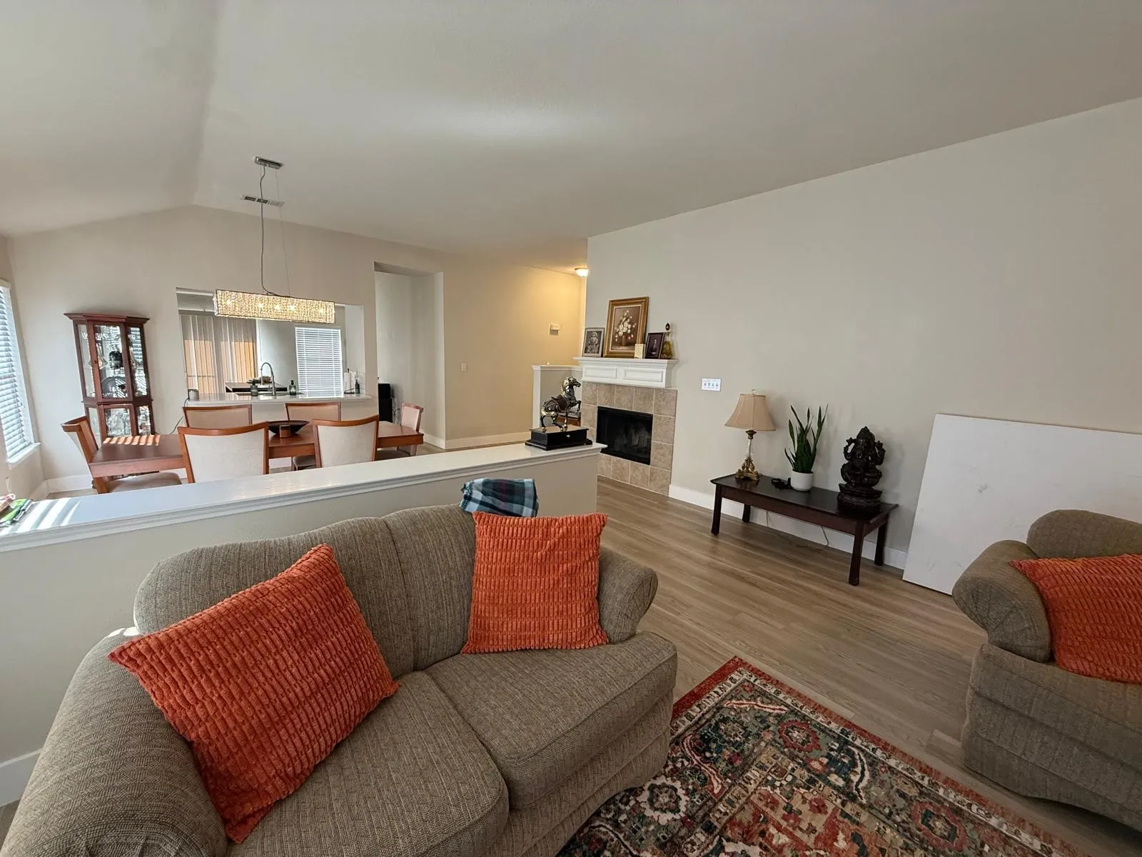Living area with light wood-finish flooring, a tile-surround fireplace, and a vaulted ceiling