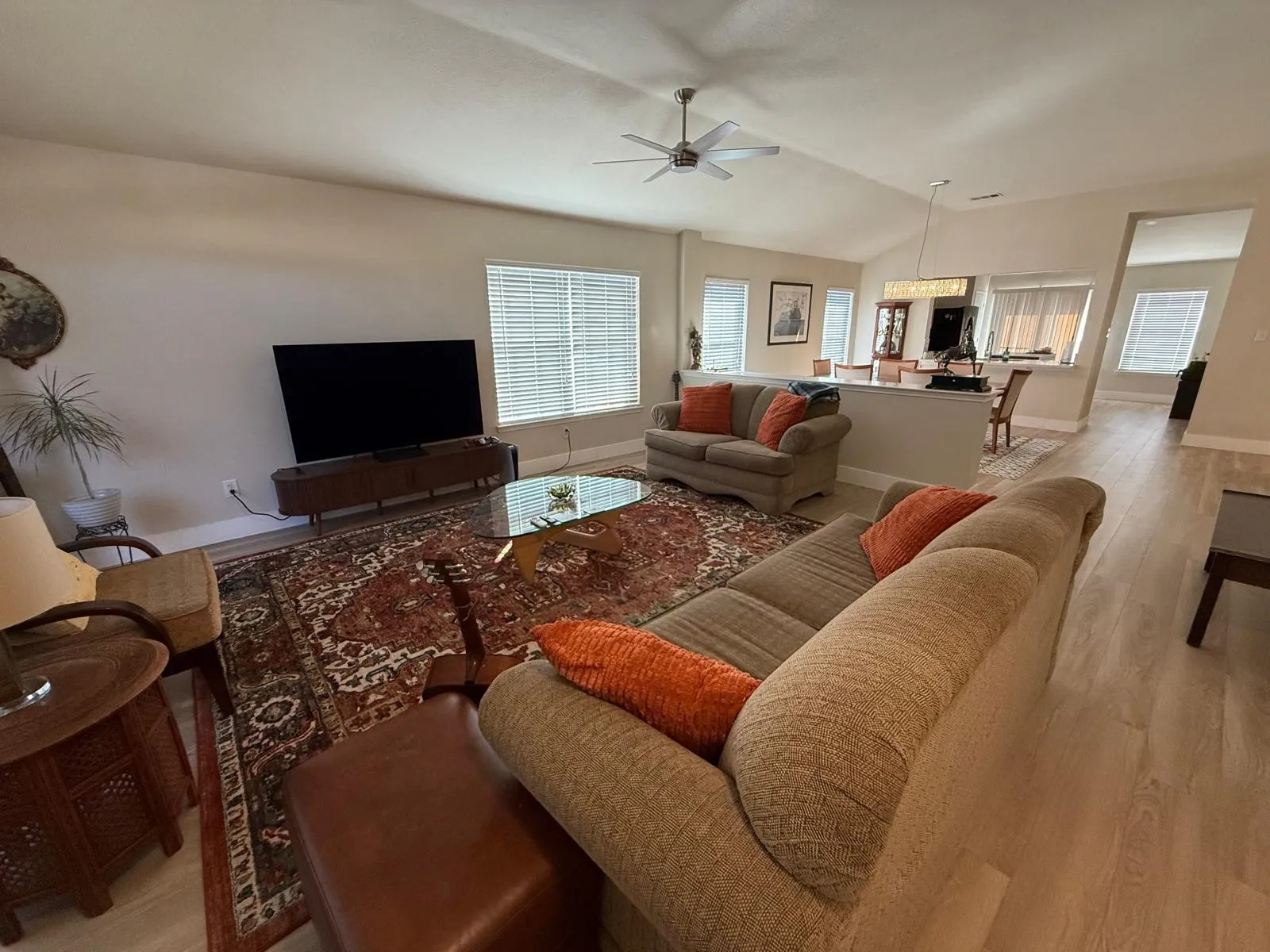 Vaulted ceiling with a ceiling fan, light-toned wood-finish flooring, multiple windows with blinds, and a built-in wall partition