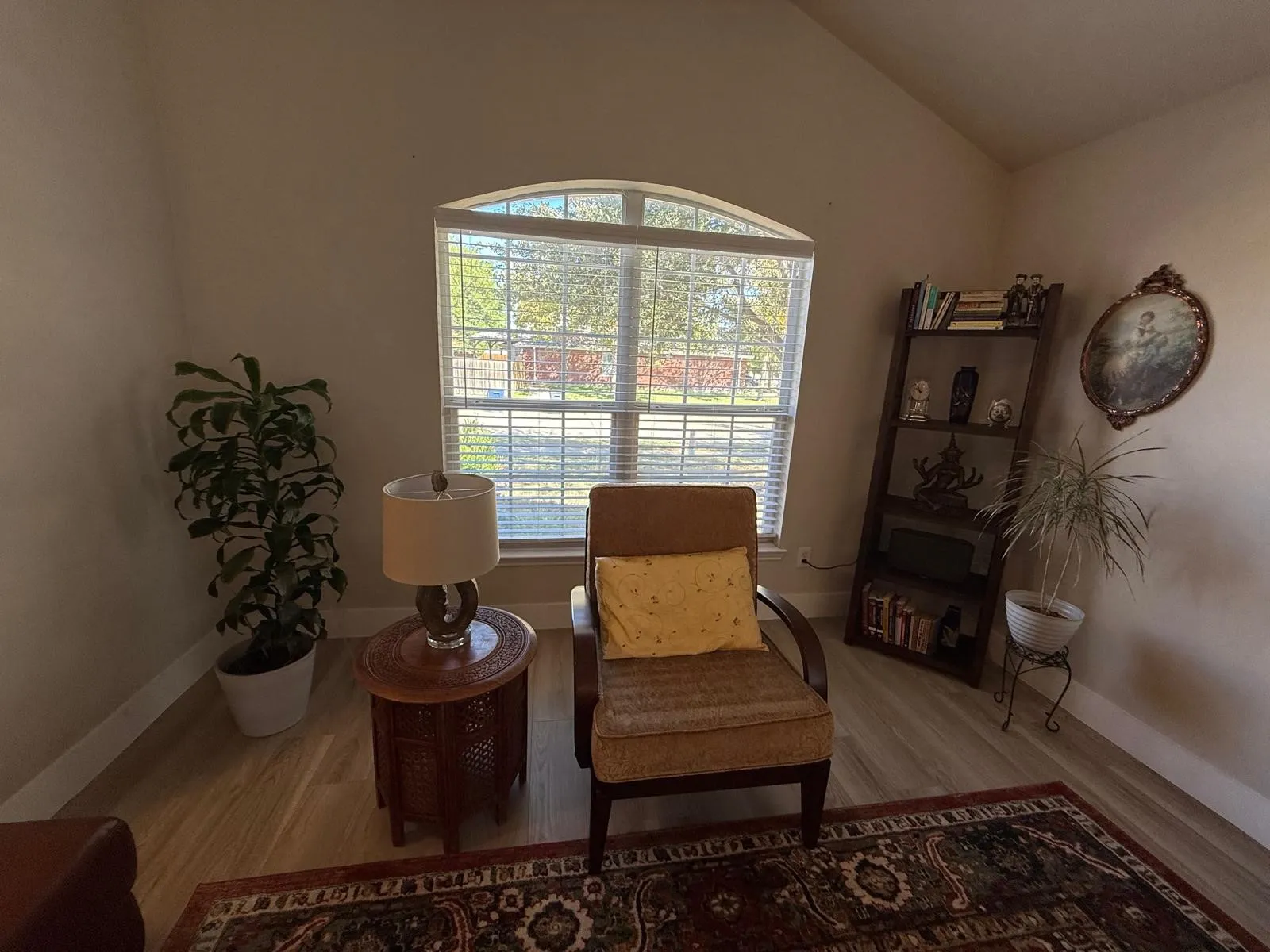 Vaulted ceiling, arched window with horizontal blinds, light wood-finish flooring, and built-in shelving