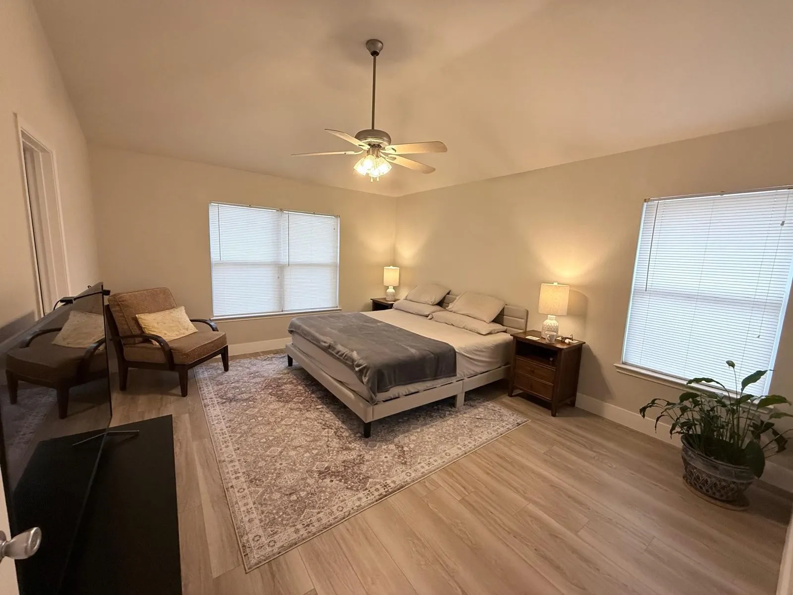 Light-toned wood-finish flooring, two large windows with blinds, and a ceiling fan with integrated lighting