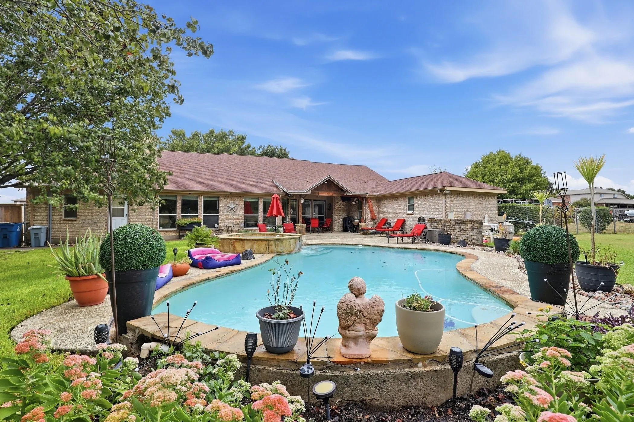 Backyard oasis featuring an in-ground swimming pool, integrated spa, stone coping, and lush landscaping