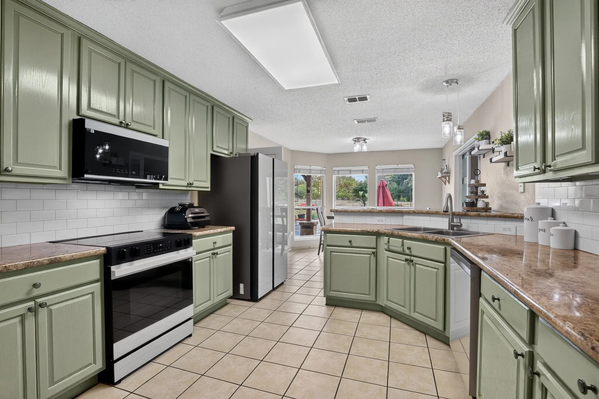 Kitchen featuring sage cabinetry, tile flooring, granite countertops, subway tile backsplash, and stainless steel appliances