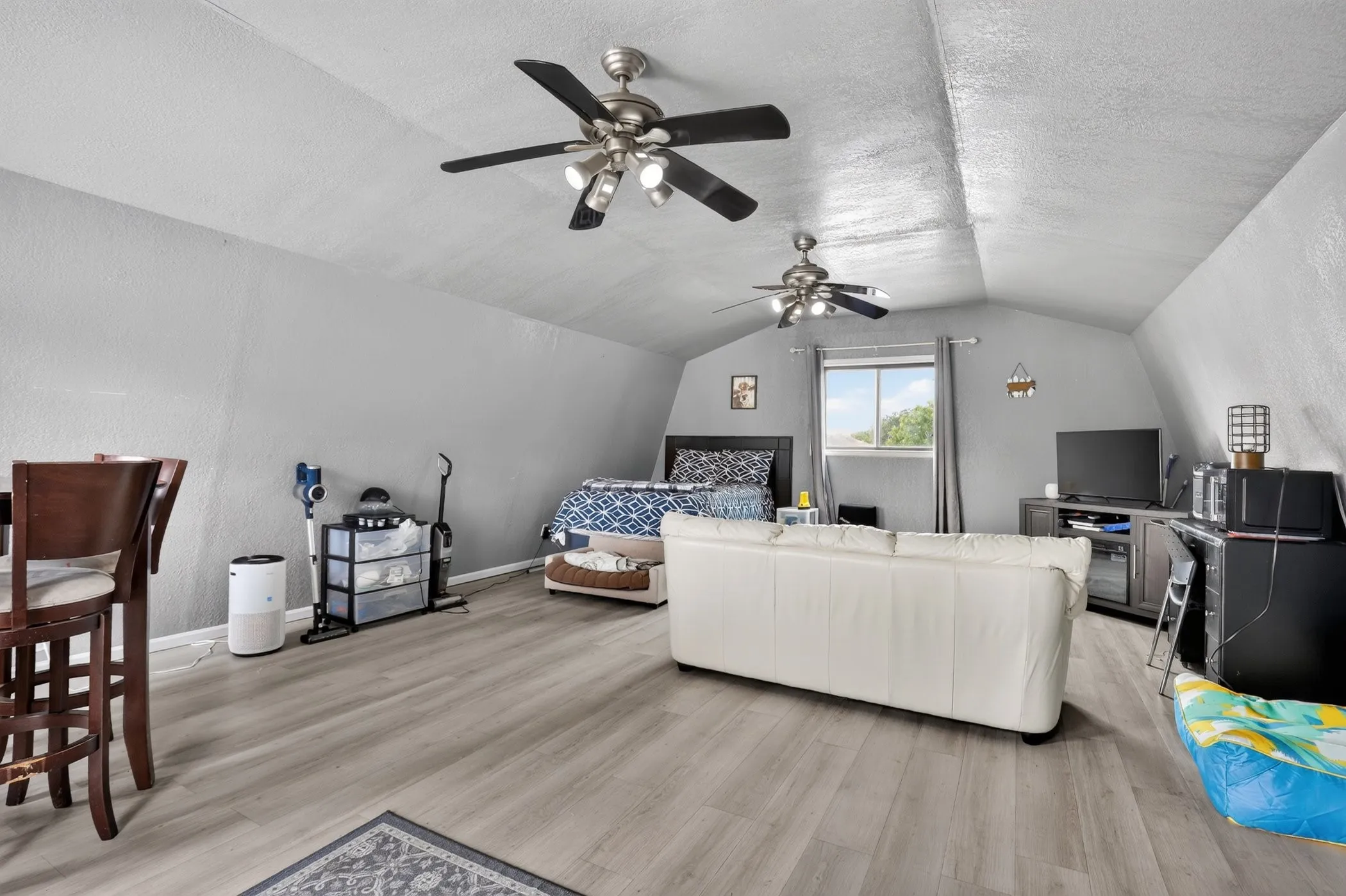 Vaulted ceiling, ceiling fans, wood-finish flooring, window with natural light, and a built-in bar-height counter
