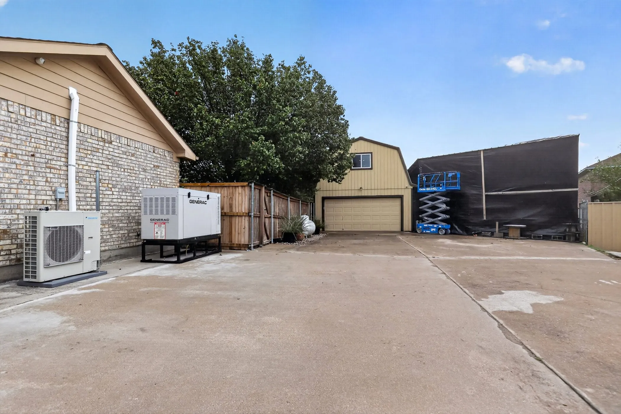 Brick exterior with vinyl siding, concrete driveway, wood privacy fence, detached garage with gambrel roof, and whole-house generator