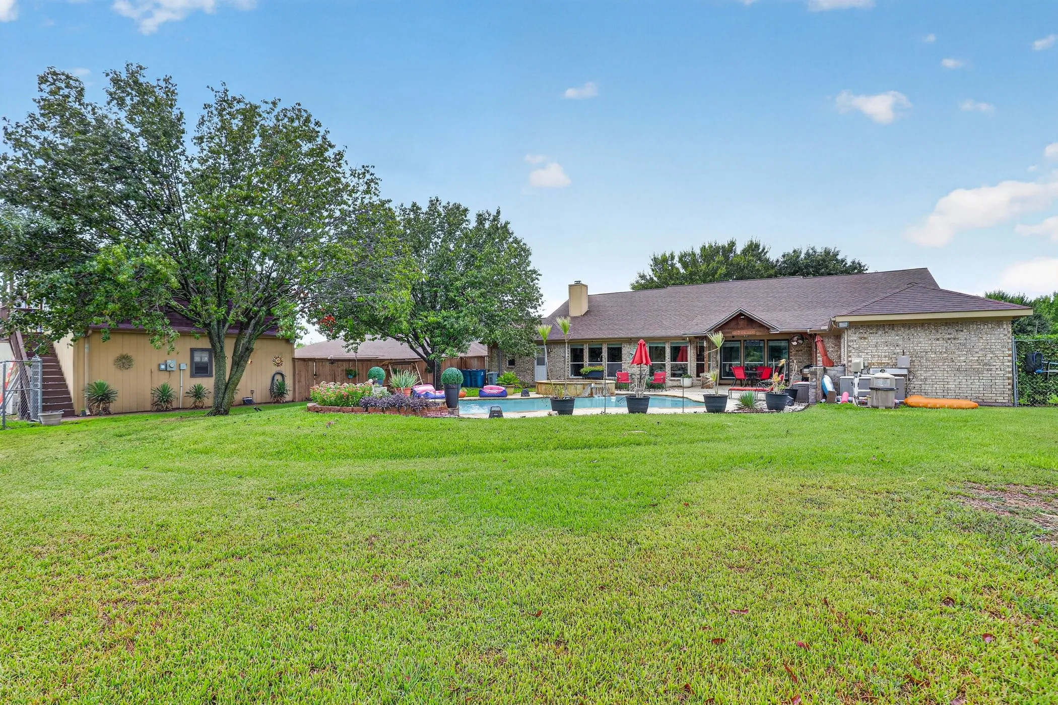 Expansive green lawn leading to a brick-clad residence with a pitched shingle roof, outdoor swimming pool, and a dedicated patio area