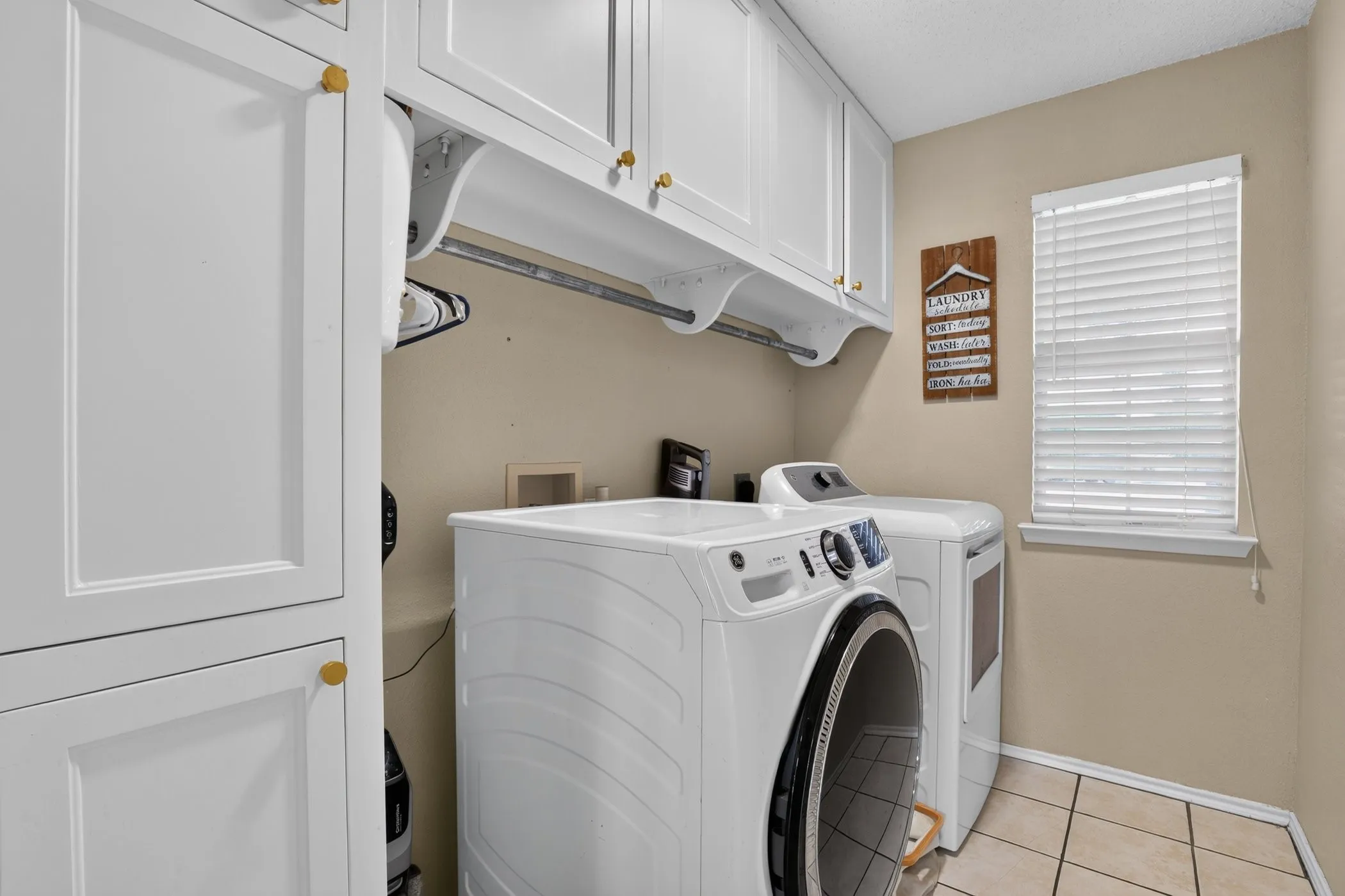 White shaker-style cabinetry with gold-tone hardware, a built-in hanging rod, and ceramic tile flooring