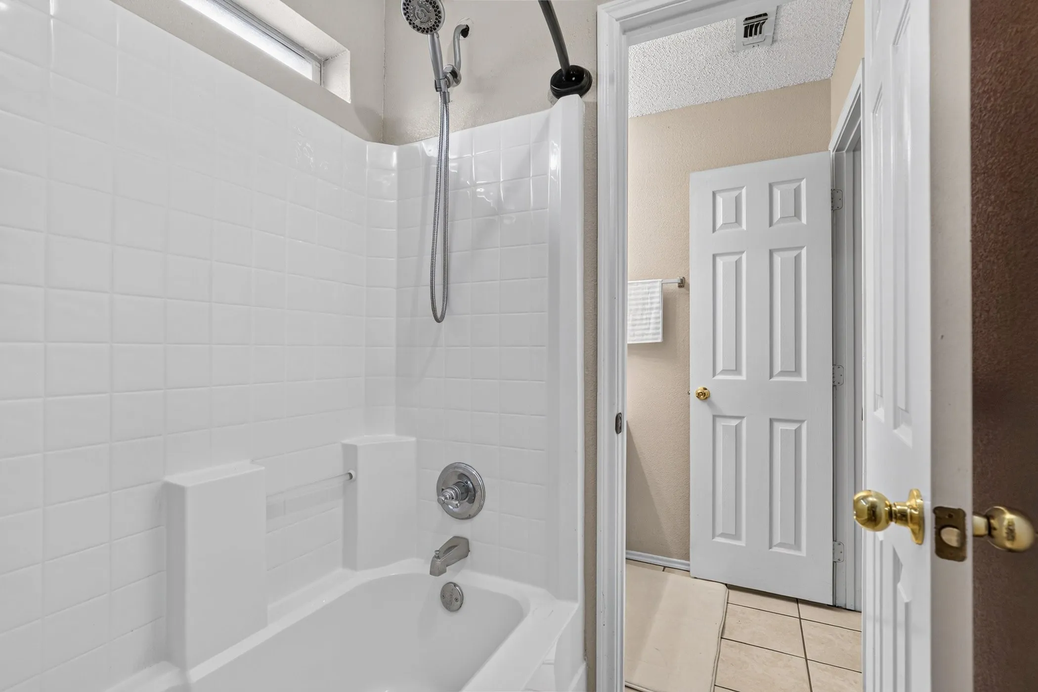 White tiled shower surround with chrome fixtures, a combination showerhead and handheld sprayer, and a small transom window