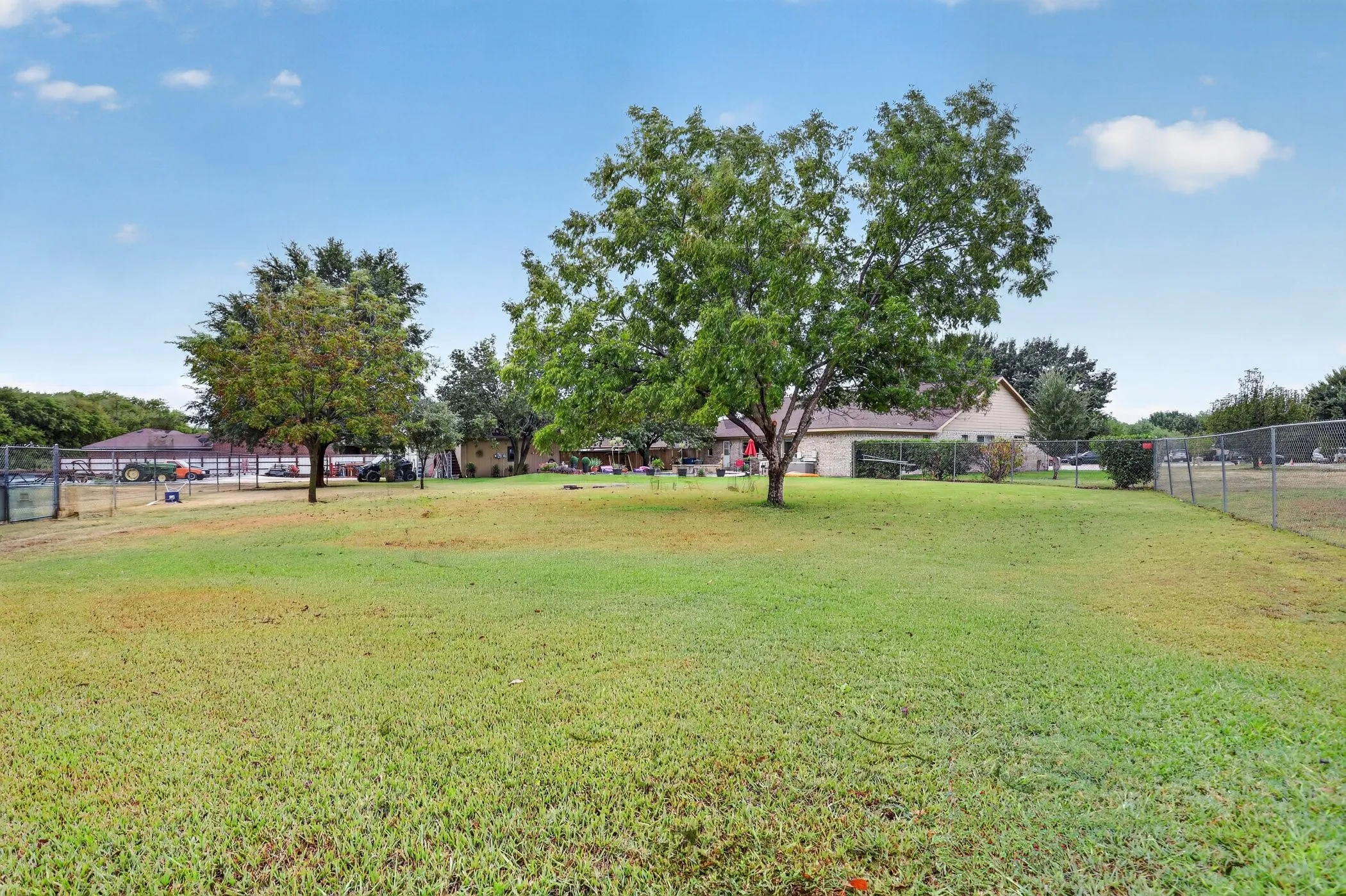 Expansive green space featuring established trees and perimeter fencing